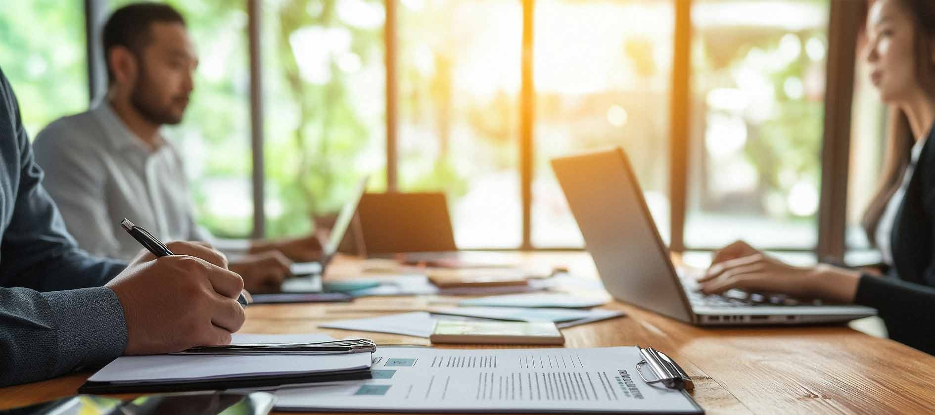 Spezialisten arbeiten gemeinsam in einem modernen Konferenzraum. Auf dem großen Konferenztisch liegen Unterlagen und Laptops. 