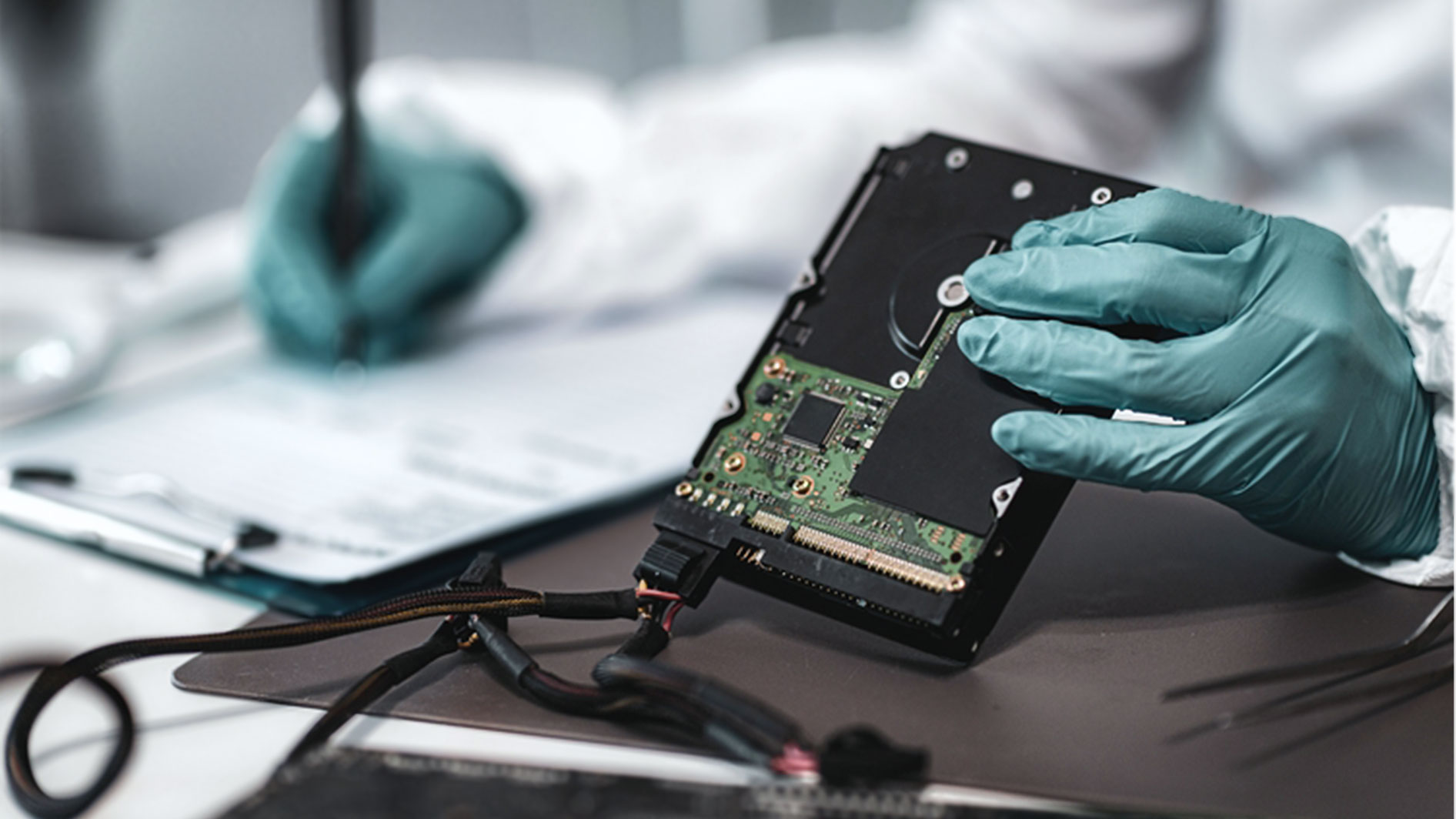 Forensiker mit Handschuhen untersucht Festplatte im Labor zur digitalen Spurensicherung
