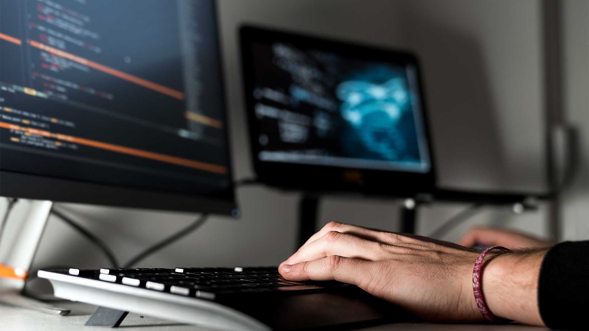 Entwickler testet Sicherheitssysteme am Computer. Quellencode Analyse erscheint am Monitor.